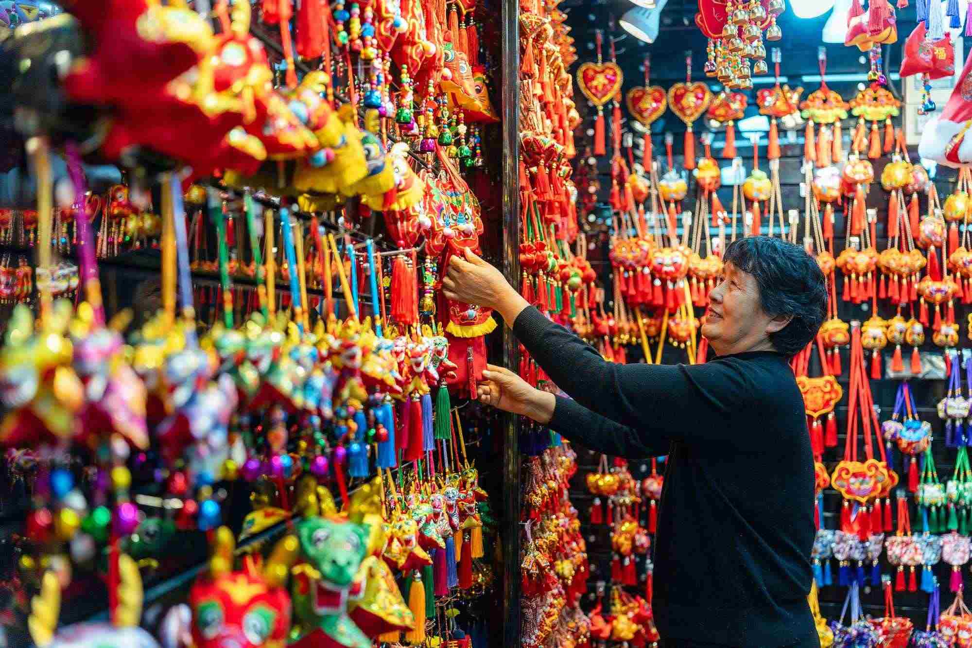 2023年12月11日，金華義烏國(guó)際商貿(mào)城，龍年喜慶用品掛滿(mǎn)攤位，顧客正在挑選中。