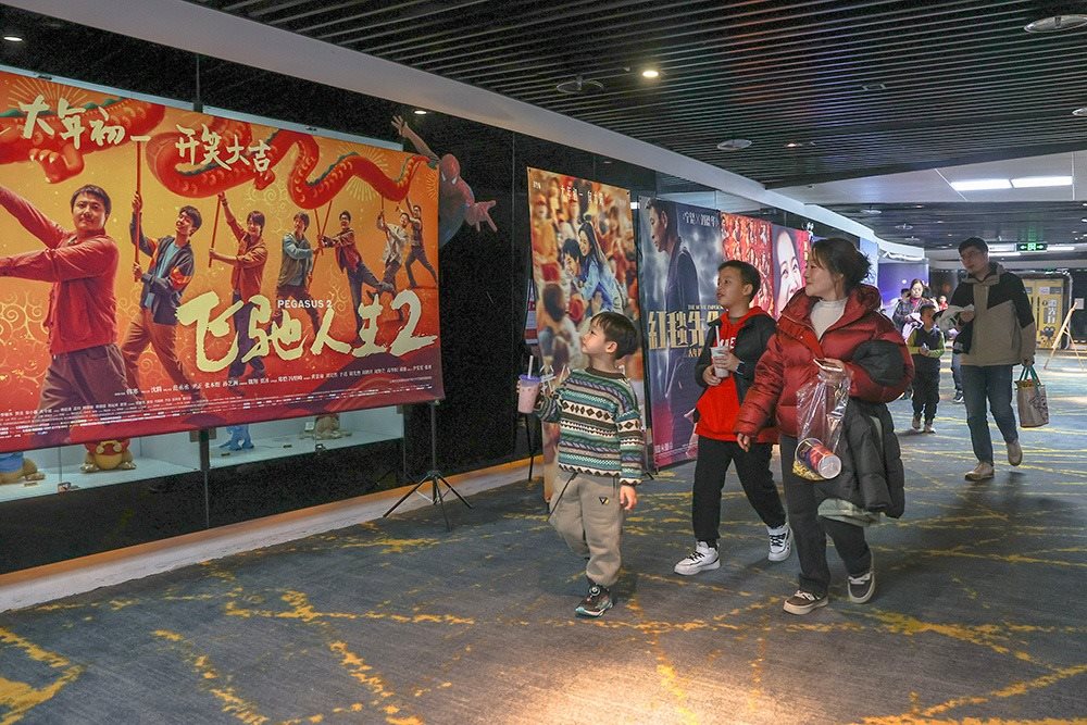 △ 2024年2月16日，在江西贛州一家電影院，觀眾從春節(jié)檔電影的宣傳展板前走過。