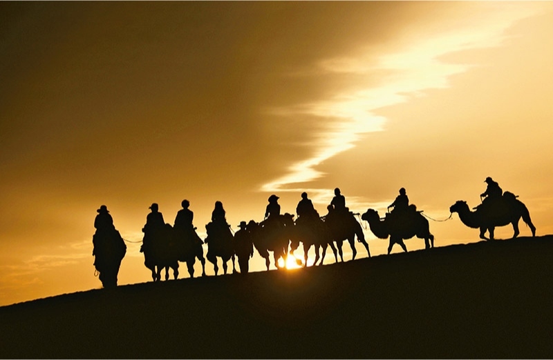 新時代以來，文化和旅游深度融合發(fā)展體制機制不斷健全，成功走出了一條獨具特色的中國旅游發(fā)展之路。圖為2024年9月1日清晨，游客在甘肅省敦煌市鳴沙山月牙泉景區(qū)乘騎駱駝，欣賞大漠風光，體驗絲路風情。 新華社發(fā) 張曉亮/攝