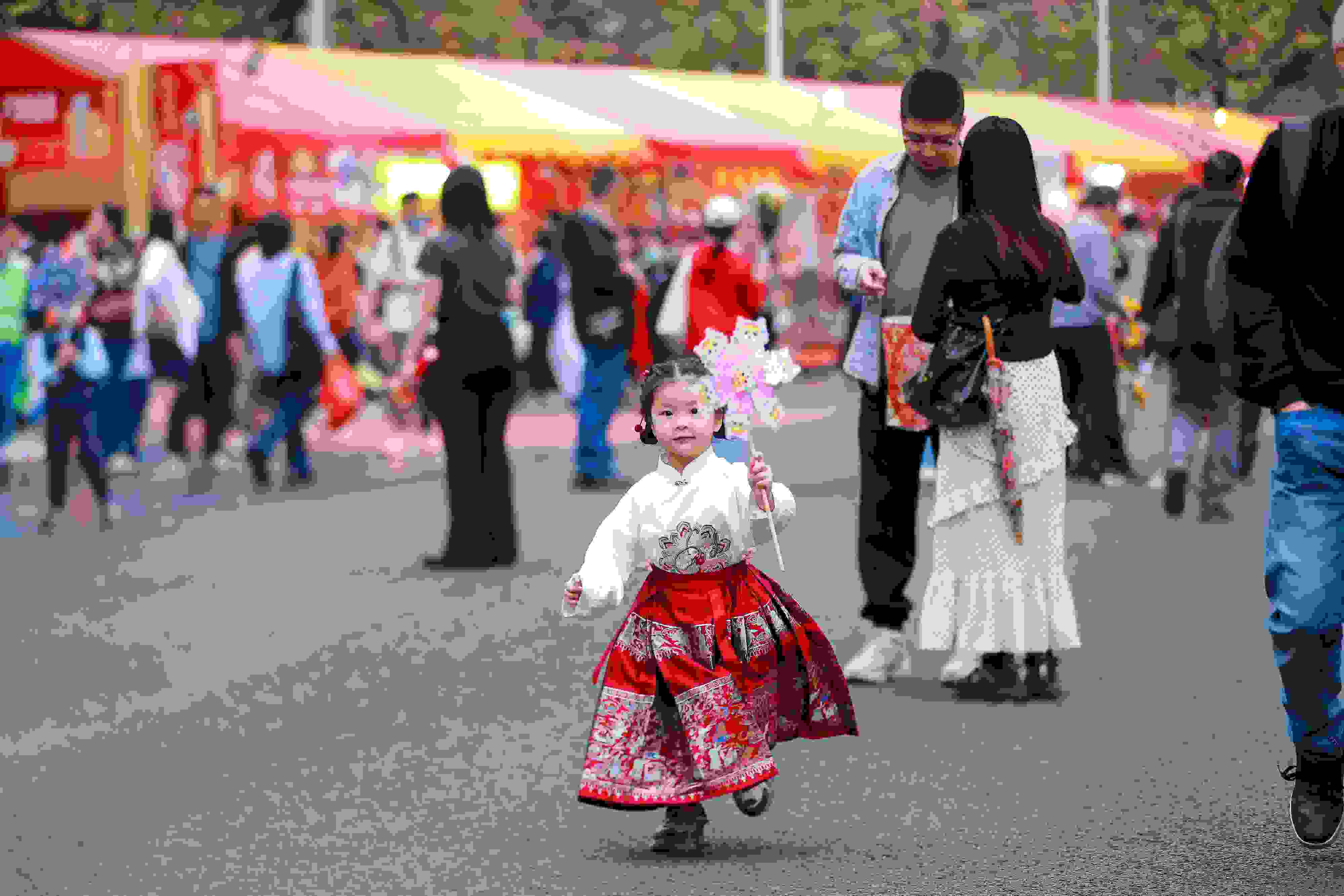 拿著風(fēng)車穿著馬面裙的小女孩在廣州的花市上開心奔跑。