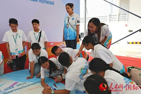 泰國學(xué)生在開營儀式展板上繪制圖案。人民網(wǎng)記者 白元琪攝